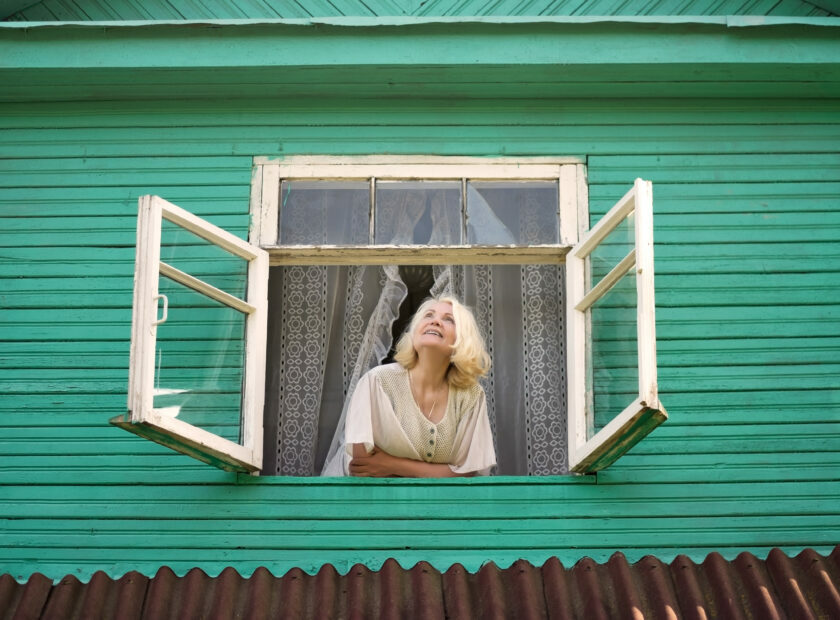 Woman near window looking up facing the sunrise at morning.