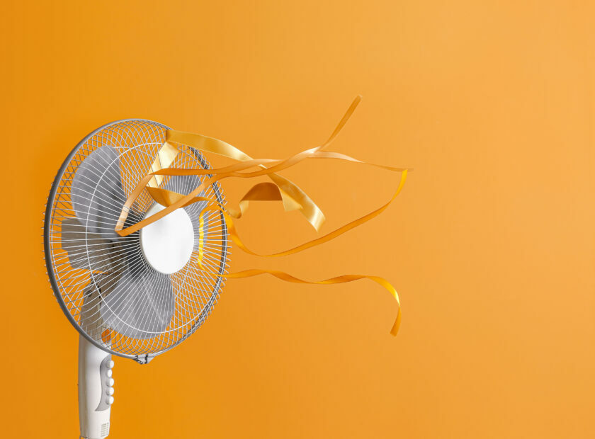 Electric fan with fluttering ribbons on color background