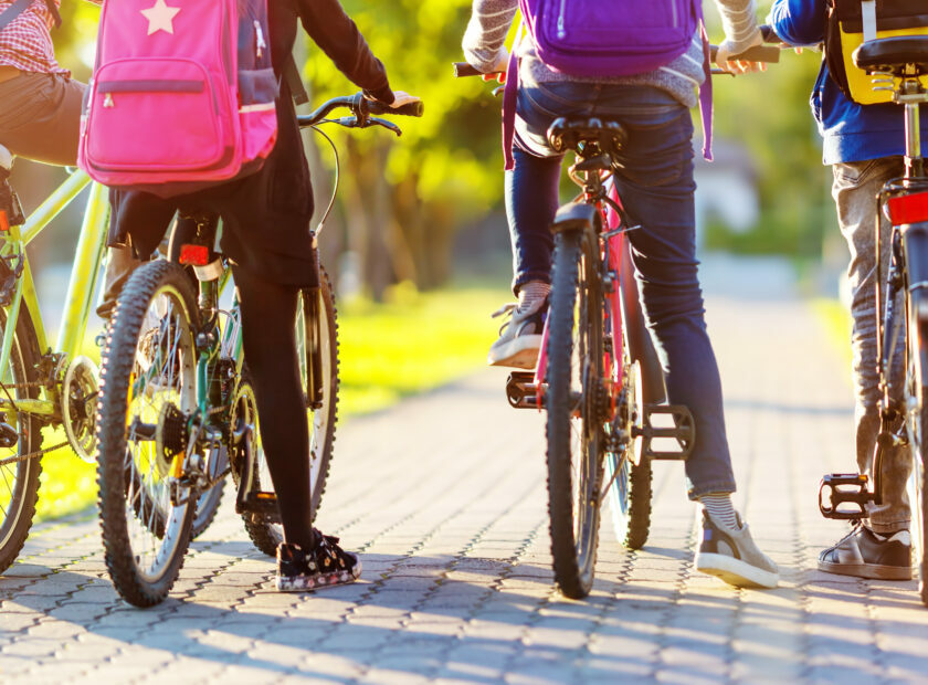 Children with rucksacks riding on bikes in the park near school