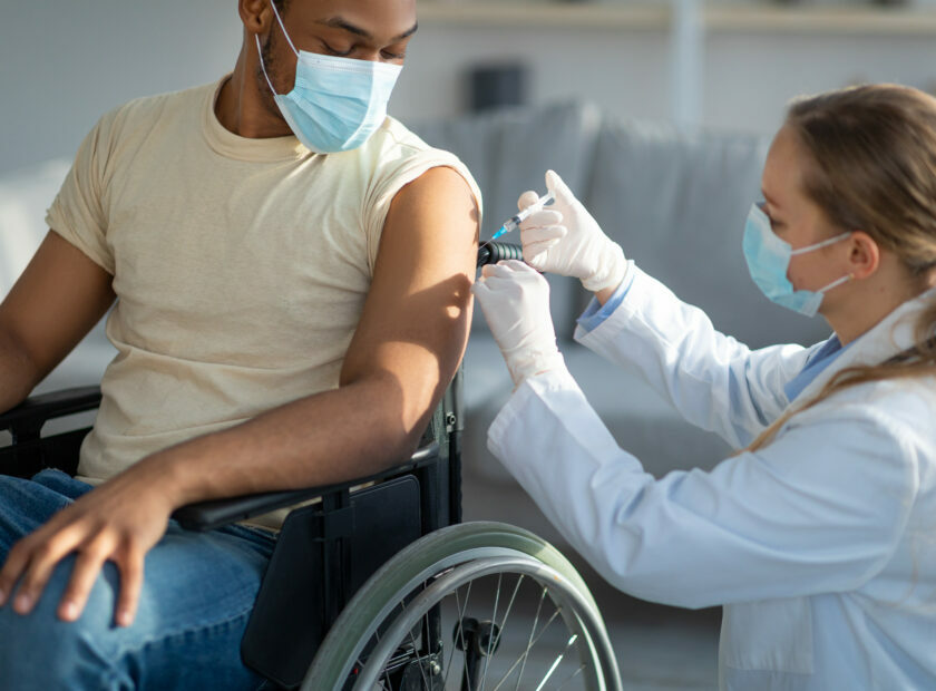 Covid-19 vaccination for homebound people. Doctor giving coronavirus vaccine to handicapped male patient in wheelchair