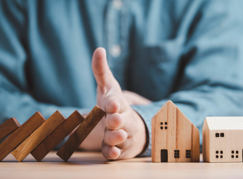 Businessman hand protect and stop wooden house from domino falli