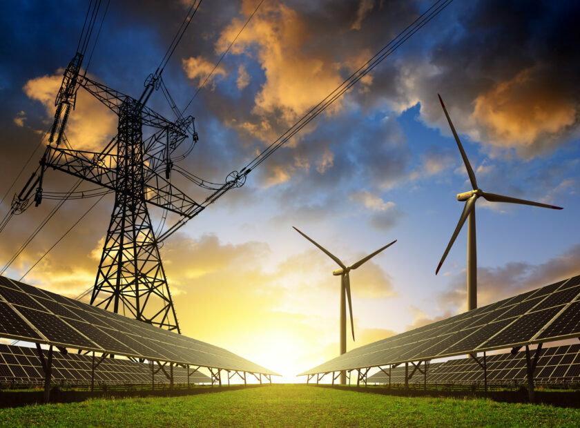 Solar panels with wind turbines and electricity pylon at sunset.